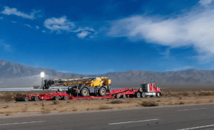 Truck hauling crane through desert highway.